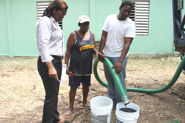 Supply Office staff Vera Brandy (left) and Tarron Slack (right) delivering molasses to livestock farmer Vera France of Camps Village at the Prospect Agricultural Station on June 07, 2015